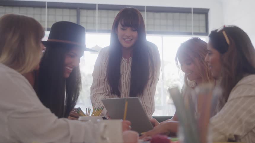 A group of women happily collaborate around a laptop in a bright office setting