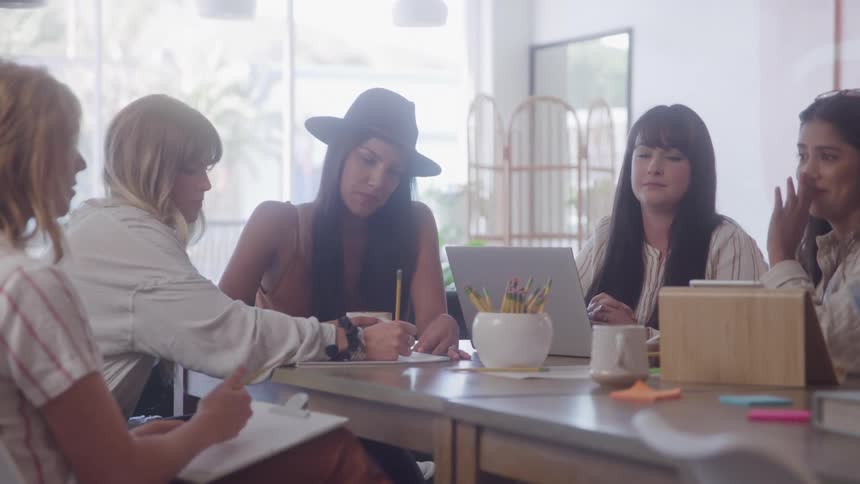 Group of women sitting around a table with a laptop and colored pencils