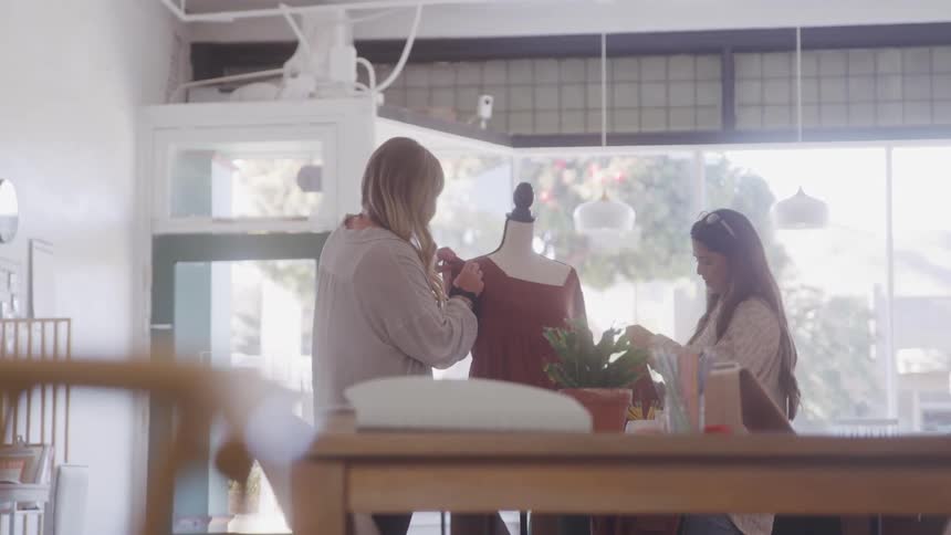 Two women putting clothes on a mannequin