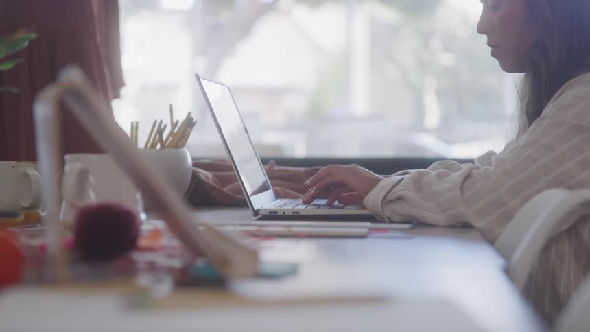 A woman types on a laptop at a brightly lit desk