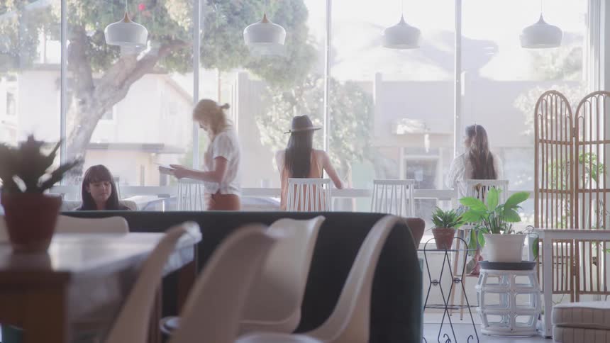 Several women interact casually inside a bright modern caf with large windows