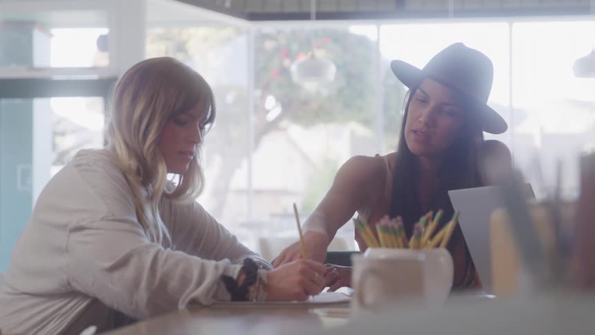 Two women talking with one of them writing something with a pencil on a piece of paper