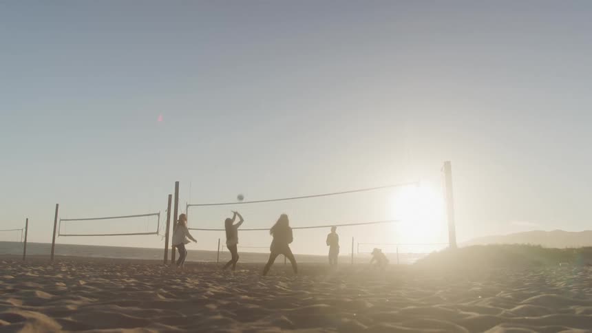 A group of people are playing volleyball on a sandy beach at sunset