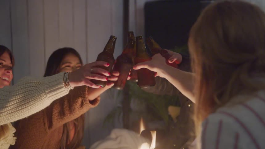 4 women toasting with beer bottles and happily gathered near a campfire