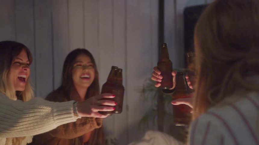 Group of girls hanging out by the fire pit toasting with beer bottles