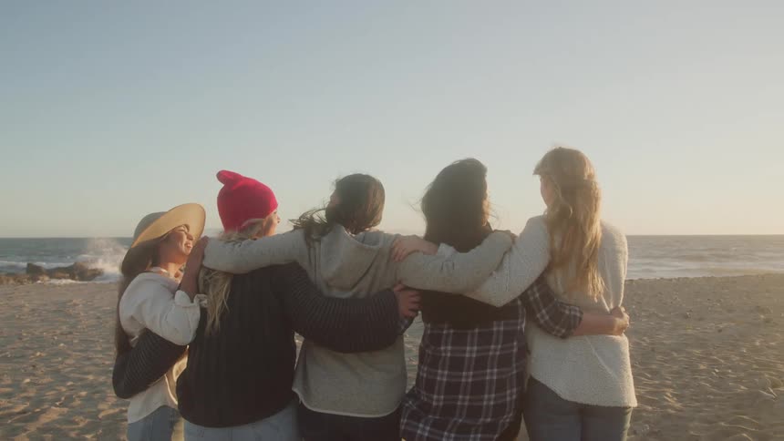 Five women hugging on the sand at the beach