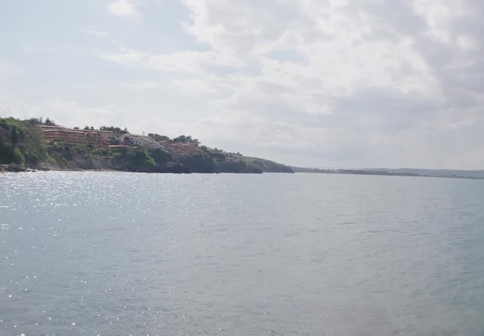 A wide scenic view of a calm coastal shoreline under a partly cloudy sky