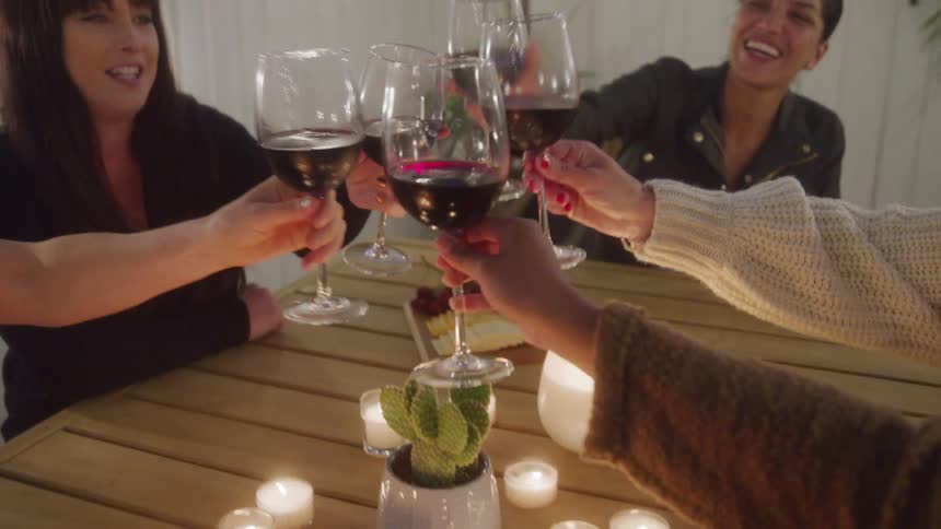 Group of friends enjoy an evening together clinking wine glasses in a cheerful toast at a cozy candlelit table