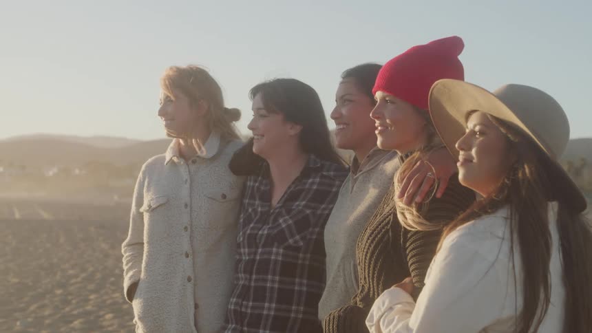 5 women gathered closely hugging each other and smiling while looking forward
