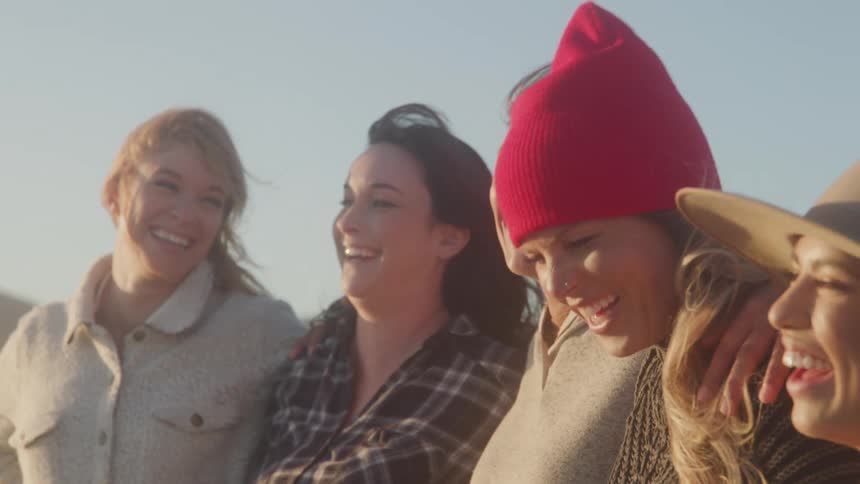 A group of women stands under the sun in a group hug with laughter and smiles on their faces