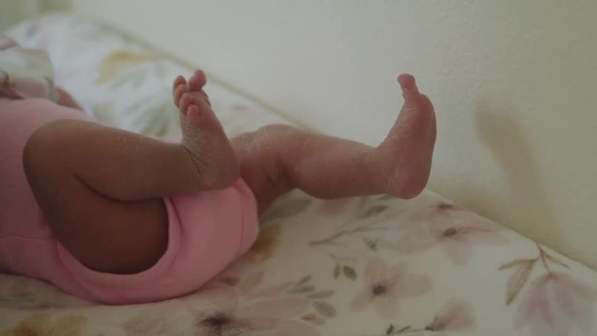 A baby lies on a floral sheet with its tiny legs and feet playfully lifted in the air