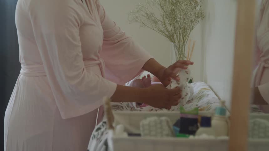 Pair of hands of an adult person changing the clothes of a lying baby