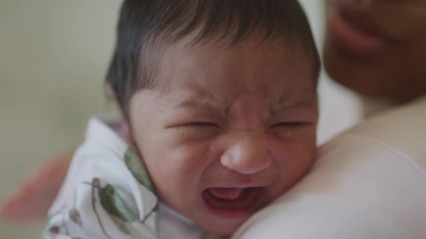 A newborn baby cries while being gently held