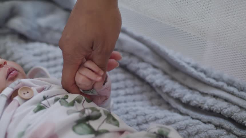 A person gently touching the hand of a baby who is in a crib