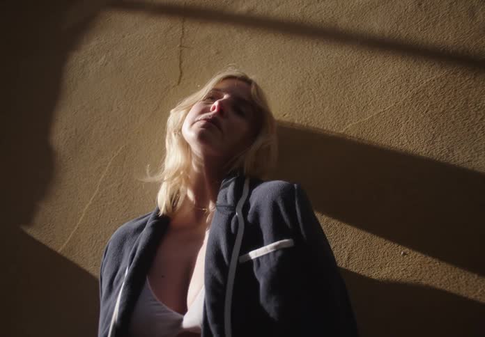 A woman poses confidently against a sunlit wall in stylish clothing