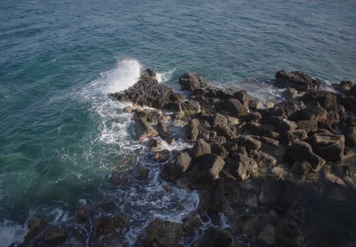 Ocean waves crash against a rocky shoreline under clear skies