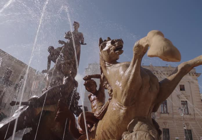 Fountain with statues of people and horses in the middle of a public square surrounded by classical buildings