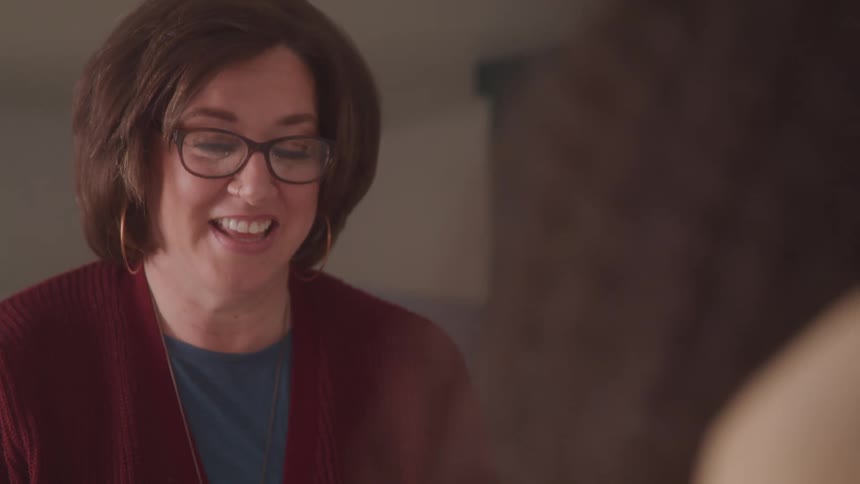 Woman with glasses with a happy expression talking to another person in front of her