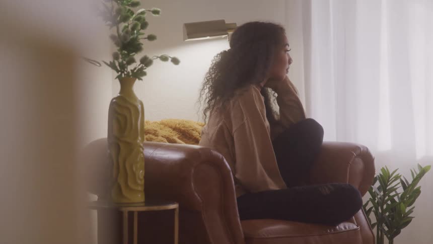 Woman sits quietly on a leather armchair gazing out the window in a cozy living room