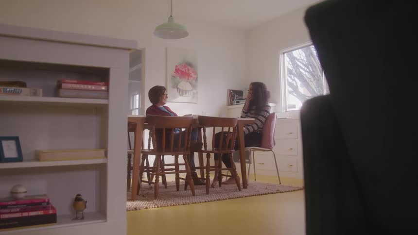A mother and daughter sit at a kitchen table enjoying a lighthearted conversation in a cozy home