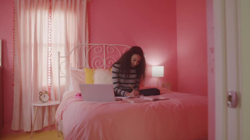 A girl sits on her bed taking notes