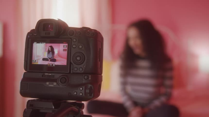 The woman is filming herself talking on the bed