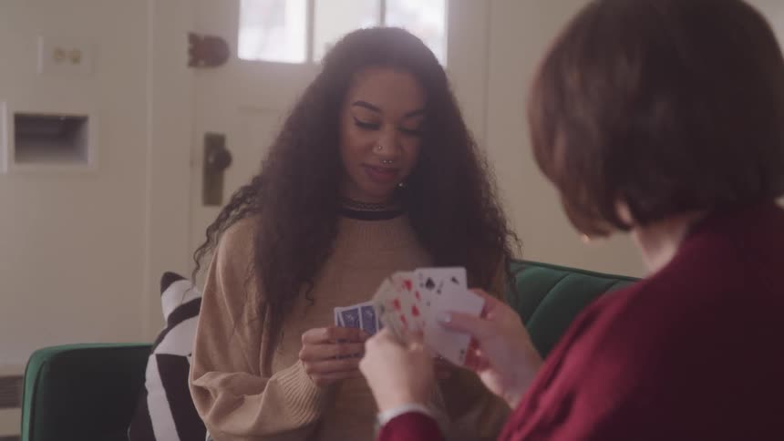 Two women seated on the couch playing cards at daytime