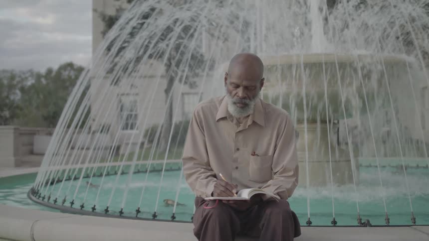 A man writing in a notebook while sitting on a fountain