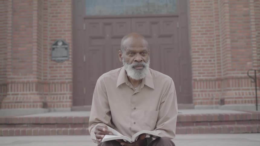 The man is reading a book outside the church