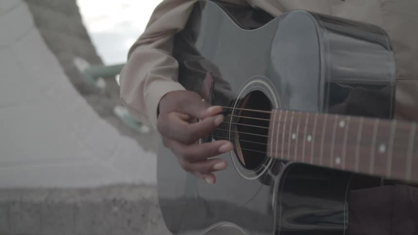 A closeup captures a person playing a black acoustic guitar