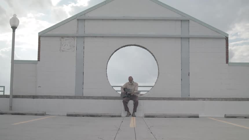 Man sitting in a square playing a guitar