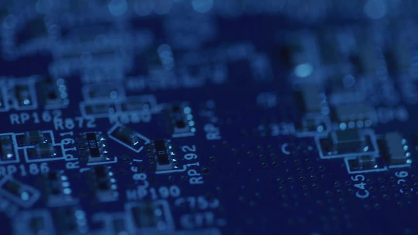 A detailed view shows a circuit board under blue lights with many small shiny components