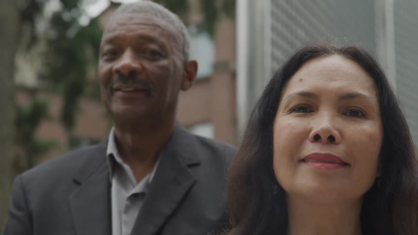A man and woman stand outdoors smiling warmly at the camera