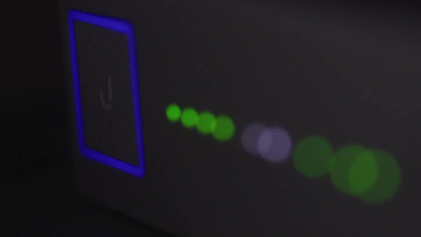 A closeup view of a power button glows blue on a smooth dark surface with blinking green lights