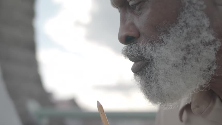 An elderly bearded man blowing on a pencil