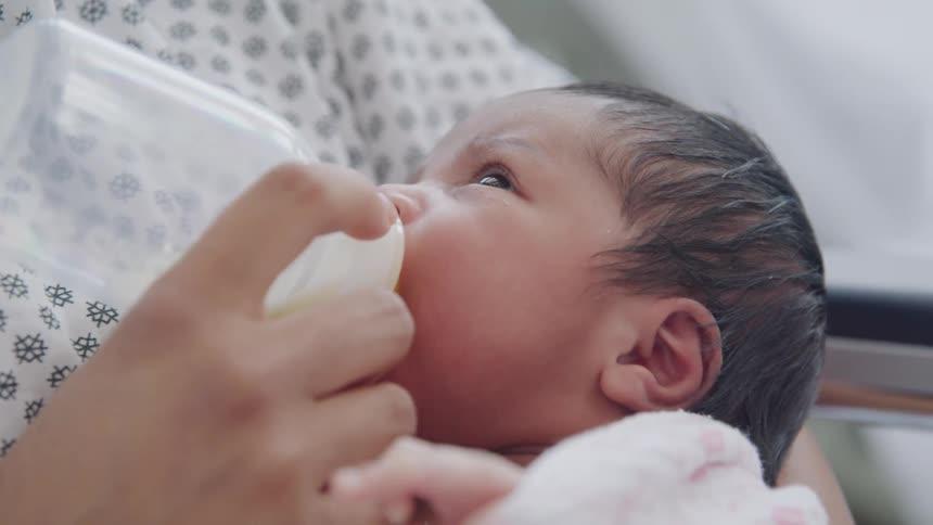 A newborn baby drinks milk from a bottle while being gently held