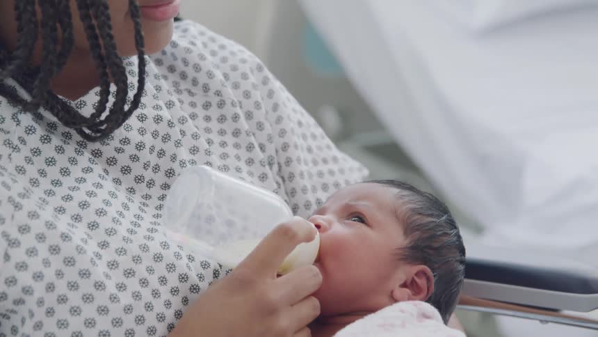 A woman in a hospital holding a newborn baby and feeding the baby with a bottle