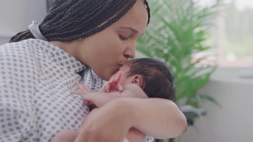 A mother holding her newborn baby in her arms kissing him on the head