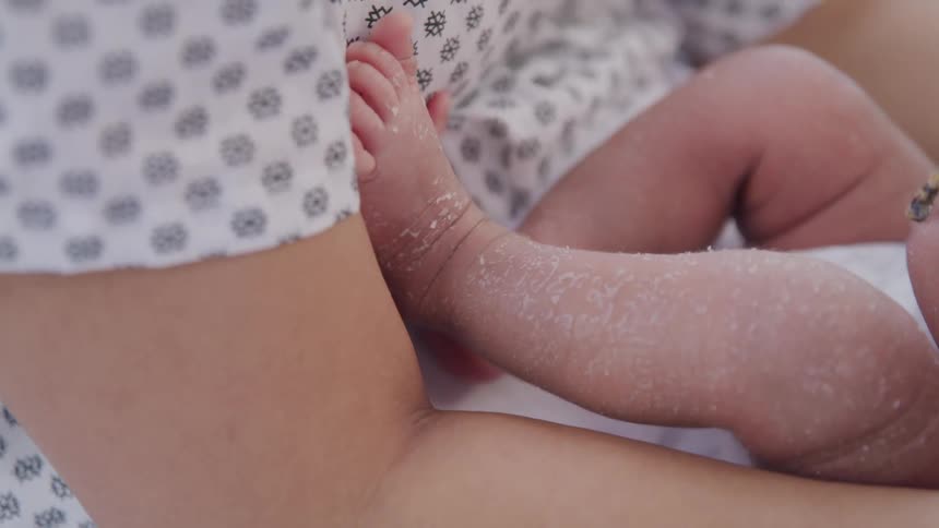 Newborn legs and feet with rest against an adults arm both clad in patterned fabrics
