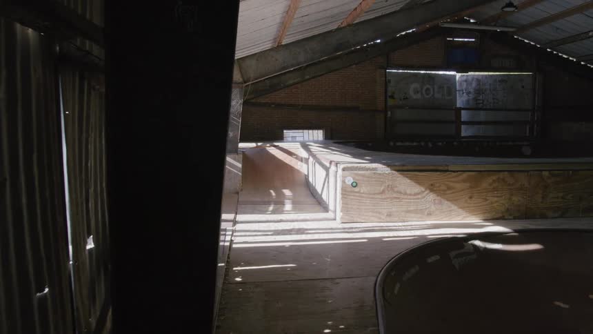 An indoor skatepark features various wooden ramps and structures under a metal ceiling