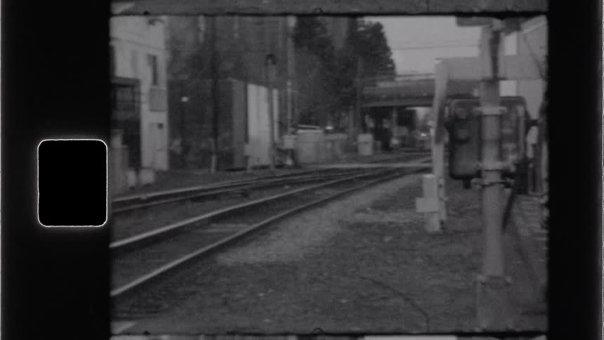 Empty railway tracks curve through an industrial area toward an overpass