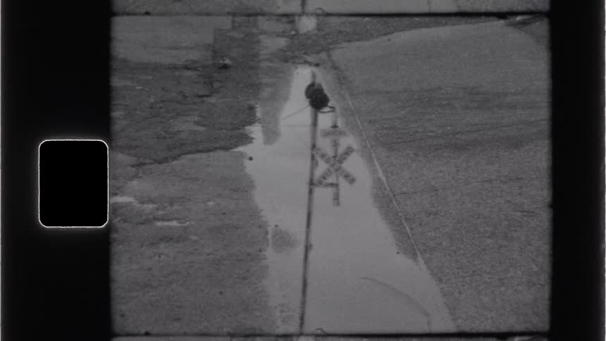 The railroad crossing sign is reflected in the puddle