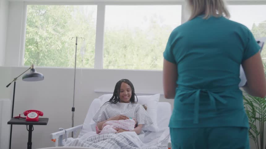 A woman who recently gave birth lies on her hospital bed as a nurse visits her around midday