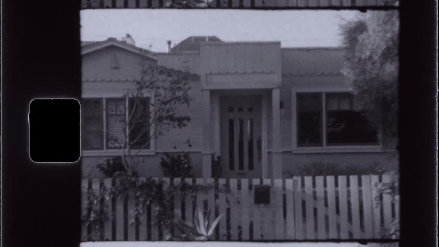 A archival frame shows a small suburban house behind a picket fence