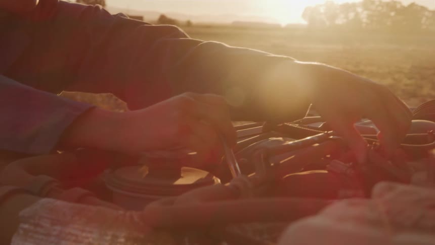 Pair of hands with a tool working on a vehicle engine outdoors