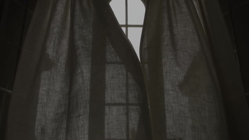 Sheer curtains billow gently in front of a tall arched window lit from behind