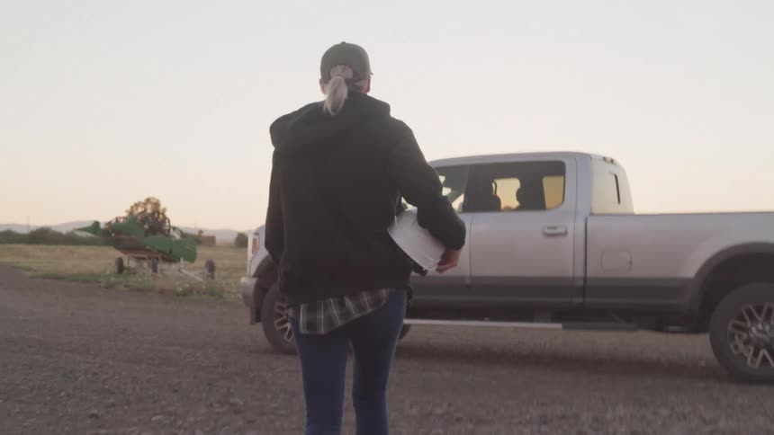 Woman holding a white helmet and walking towards a pickup truck