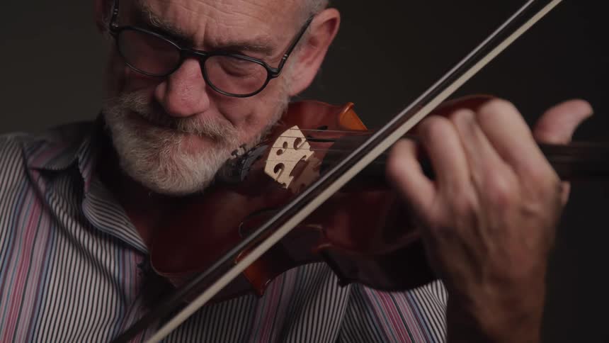 Elderly man plays violin with focused expression