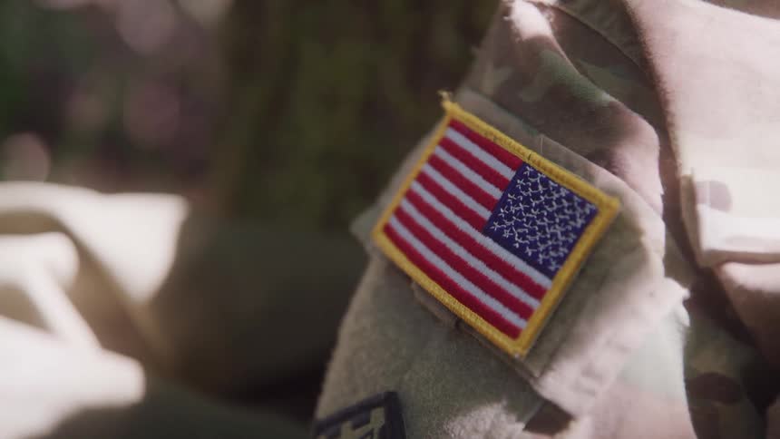 A military officer sits under the sun around midday with the usa flag badge visible on the uniform