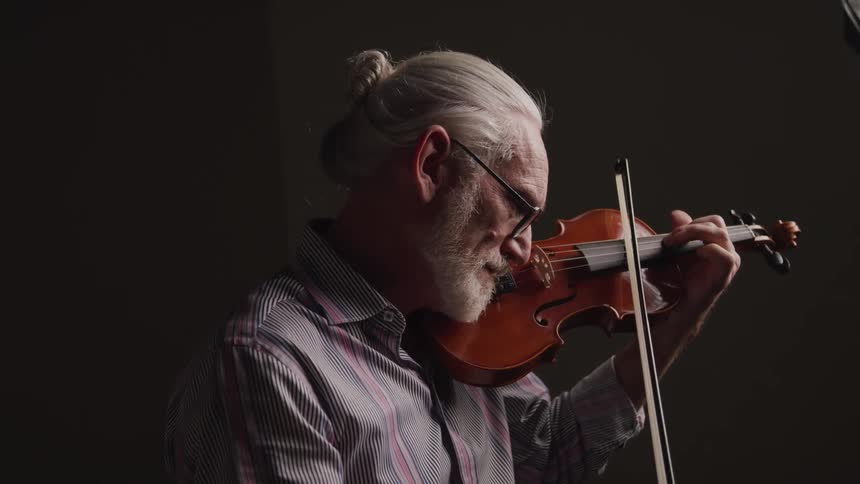 Close up of an elderly man playing a violin in a room